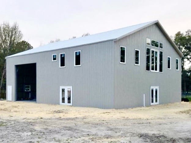 Gray metal building with white trim and multiple windows, in a rural setting.