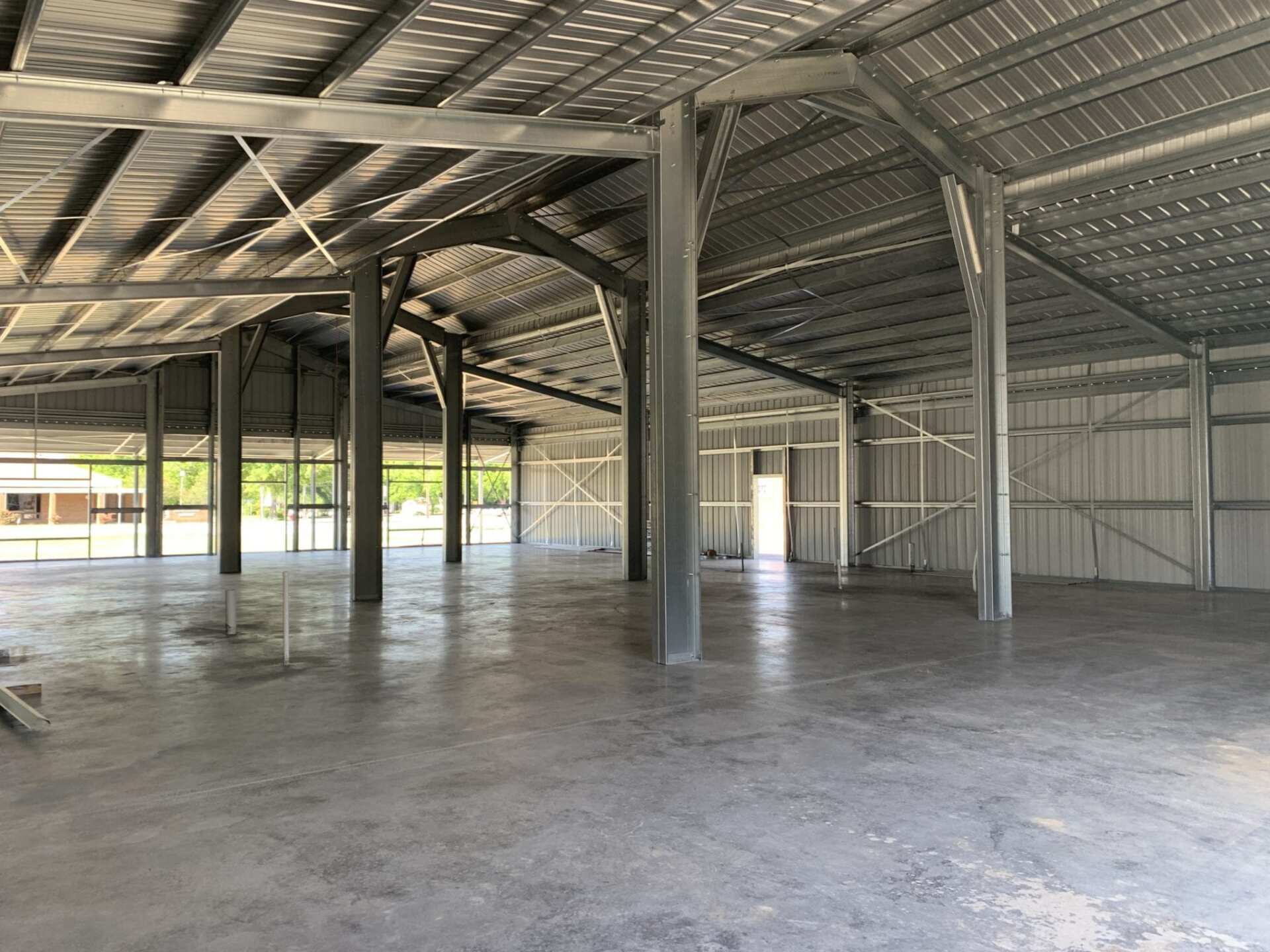 Interior view of an empty, metal building with a concrete floor and large open windows.