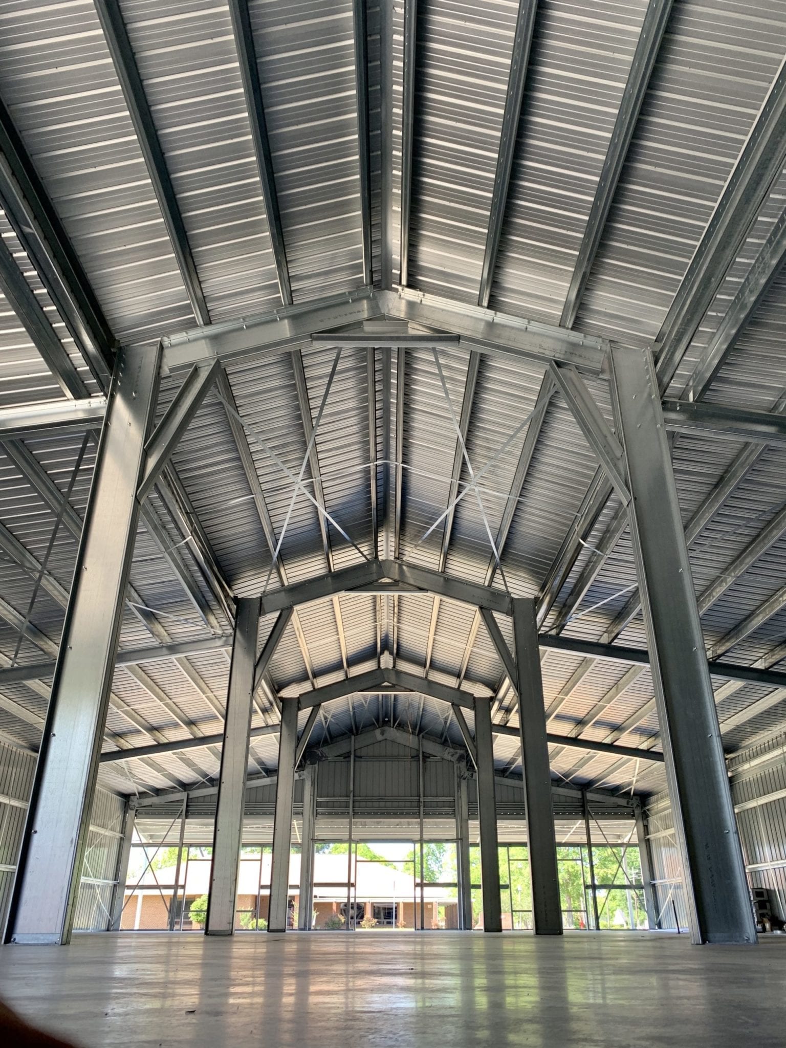 Inside a large, open metal-framed building with a concrete floor and a domed ceiling, sunlight visible at the far end.