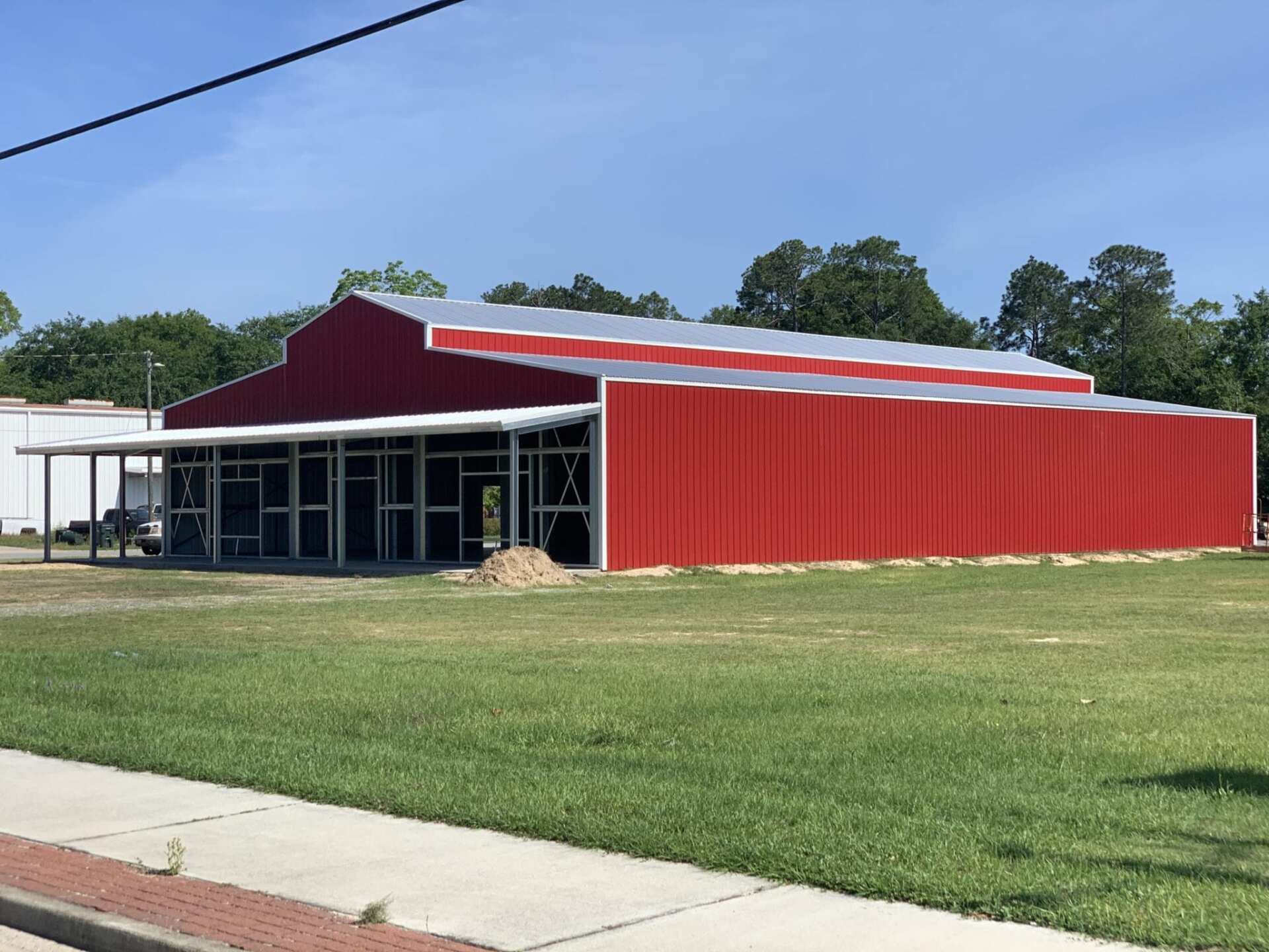 Red barn-like building with silver roof and screened porch on green lawn under blue sky.