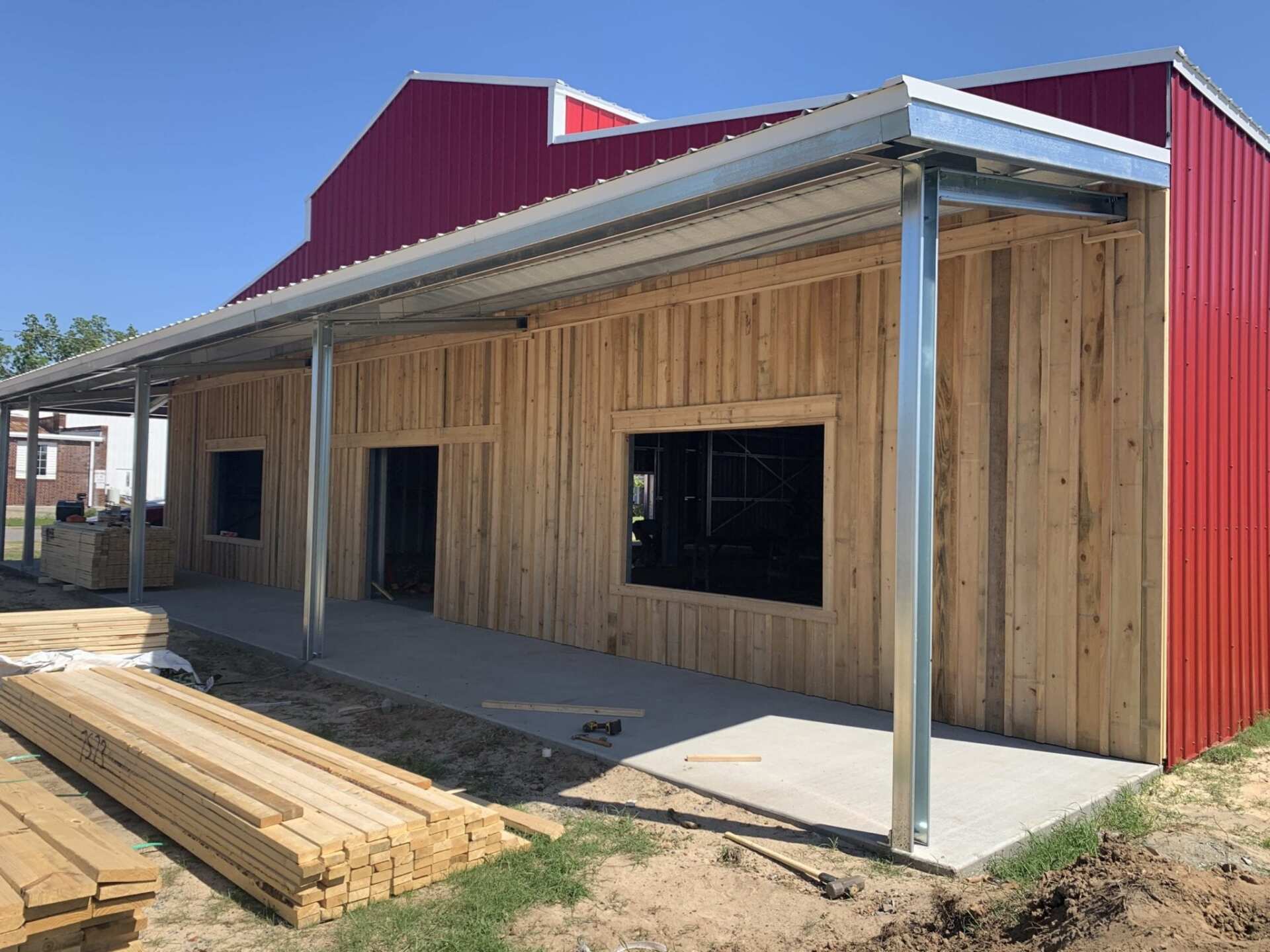 Building exterior under construction; red metal roof, light wood siding, concrete porch.