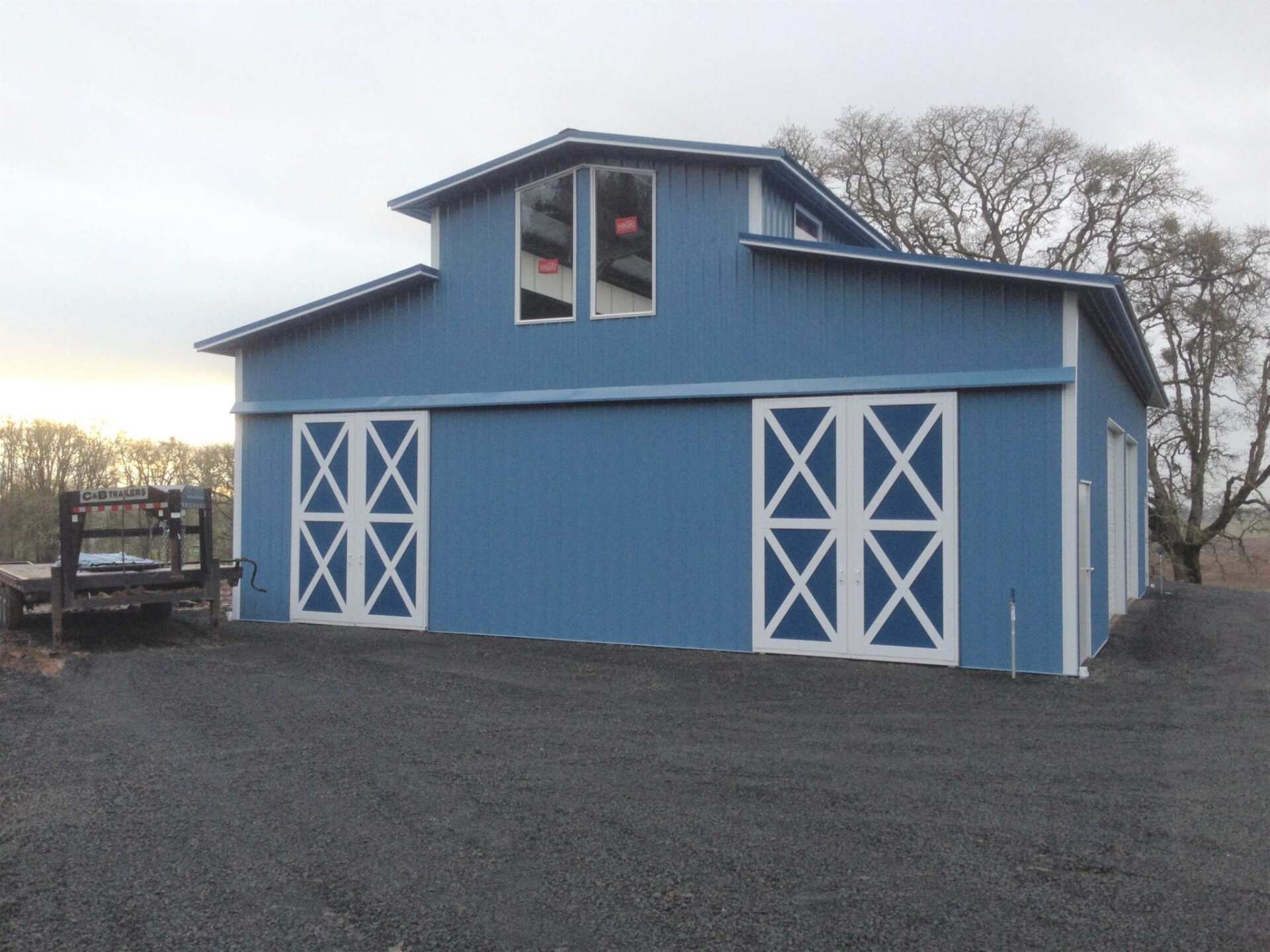 Blue barn with white doors, two-story design, set on a gravel drive, cloudy sky.