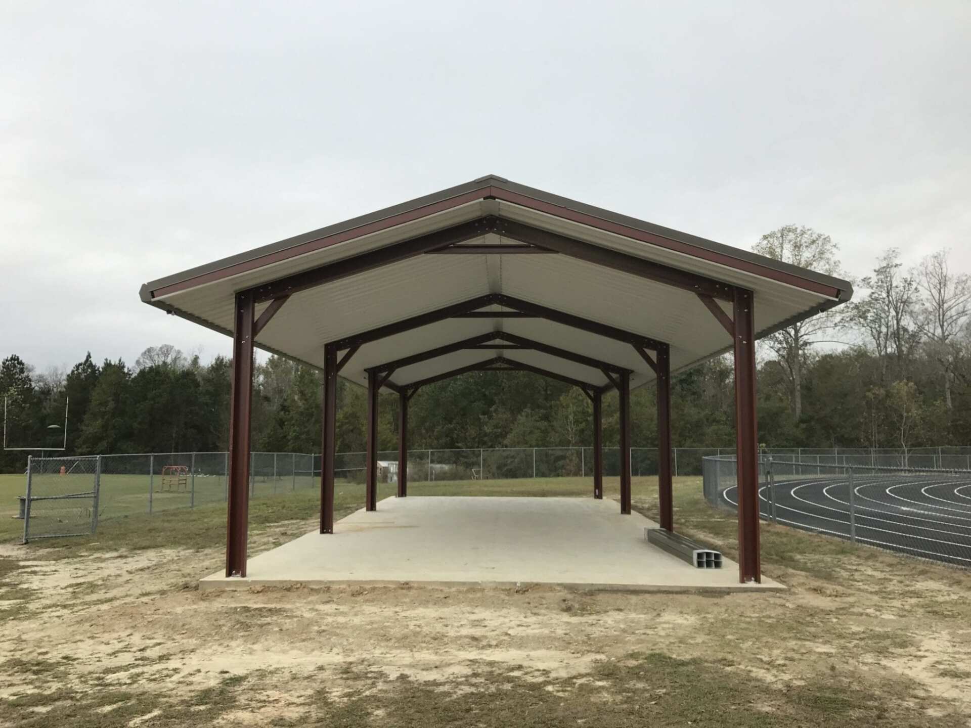 Metal shelter with a brown roof and supports on a concrete base, in a grassy field.