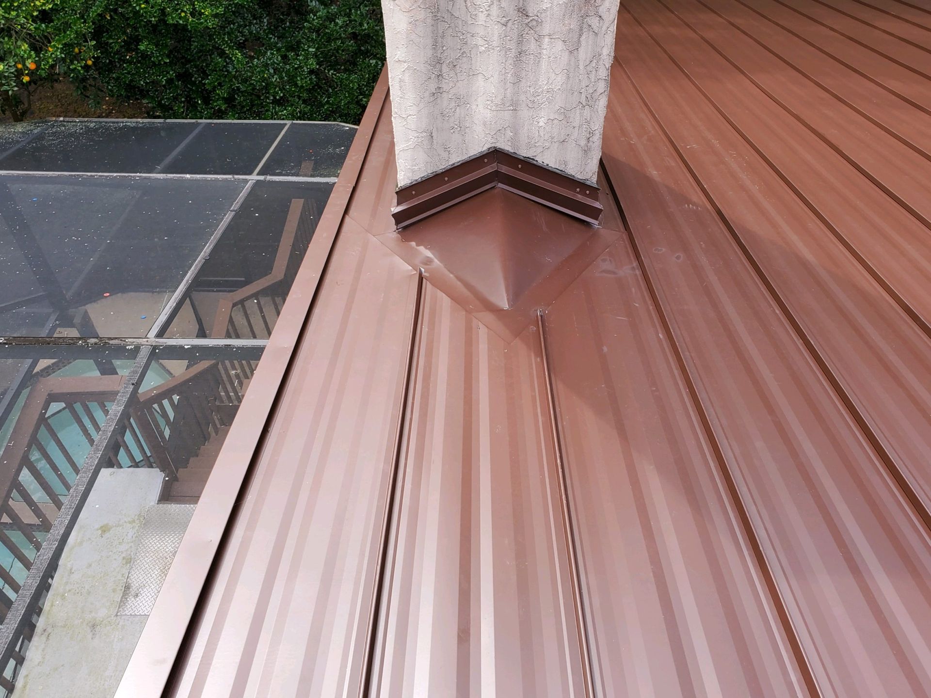 Brown metal roof with a chimney and a glass-covered structure in the background.