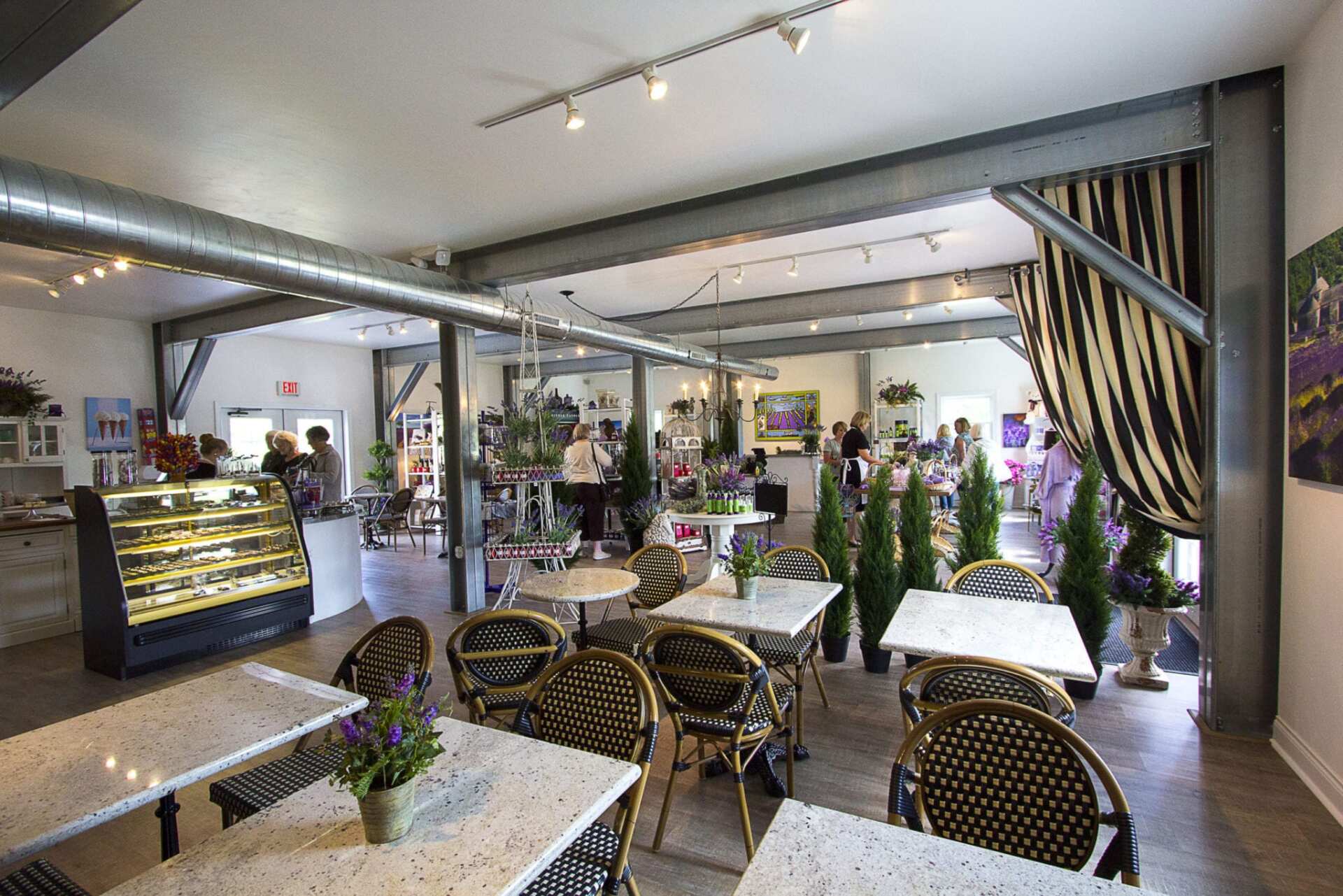 Interior of a cafe: tables and chairs, food display, people, and decorative plants.