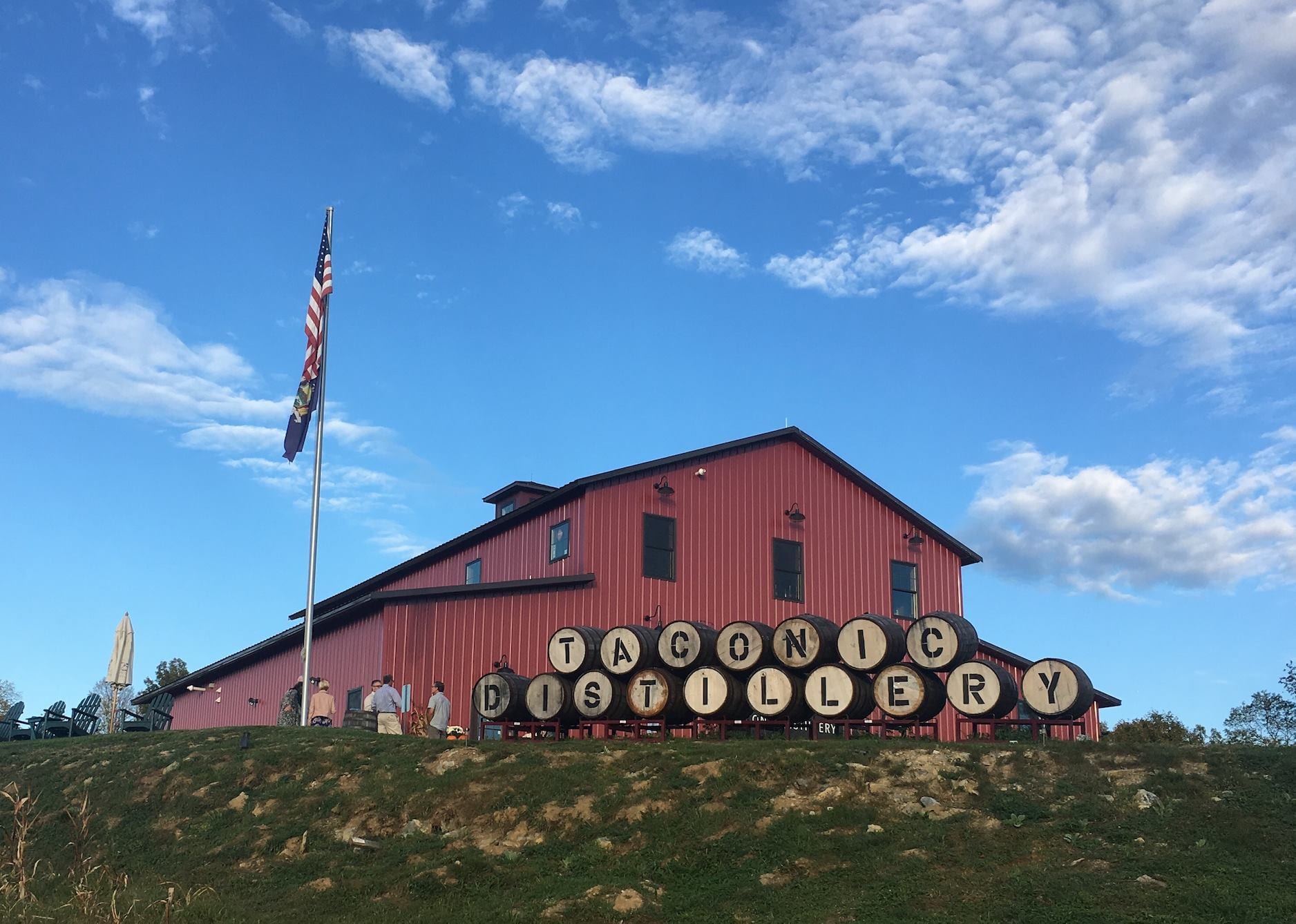 Taconic Distillery, red barn, whiskey barrels, blue sky, American flag.