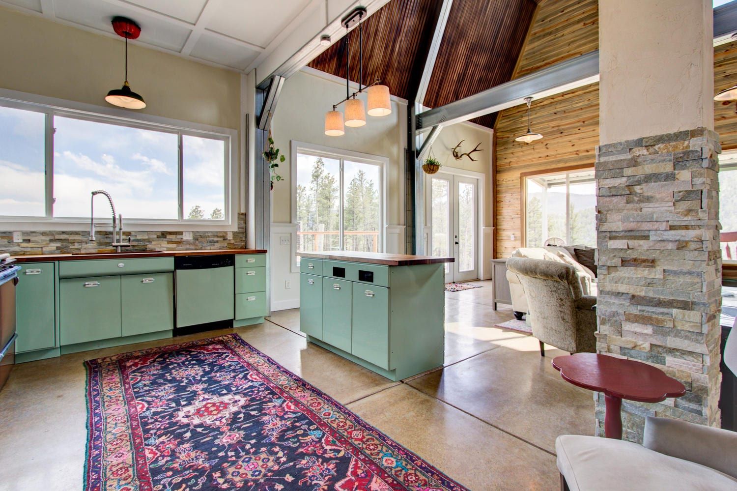Kitchen with green cabinets, island, and a patterned rug. Interior shot with sunlight and stone accents.