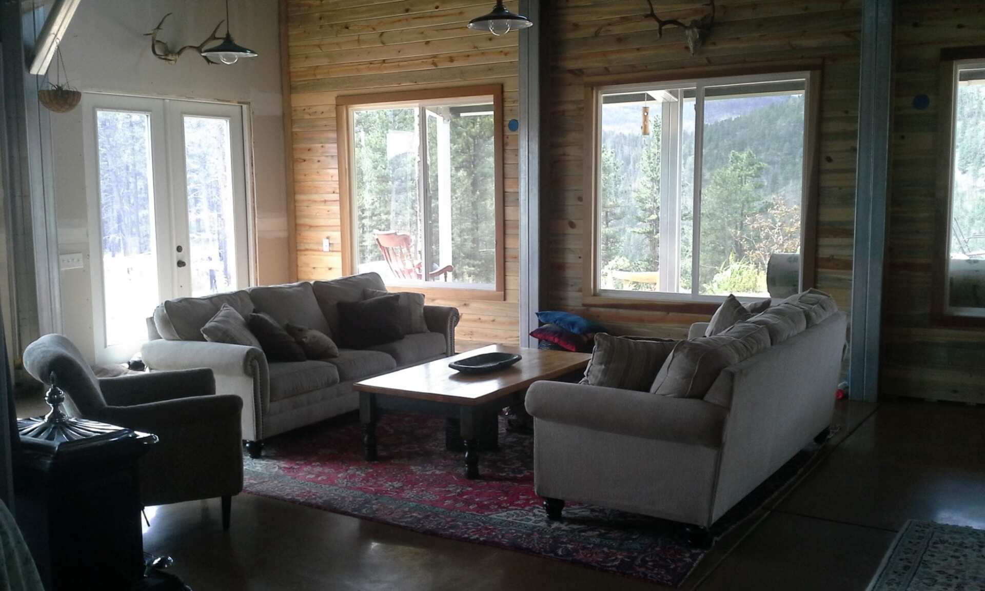 Living room with wooden walls, sofas, area rug, and large windows overlooking greenery.