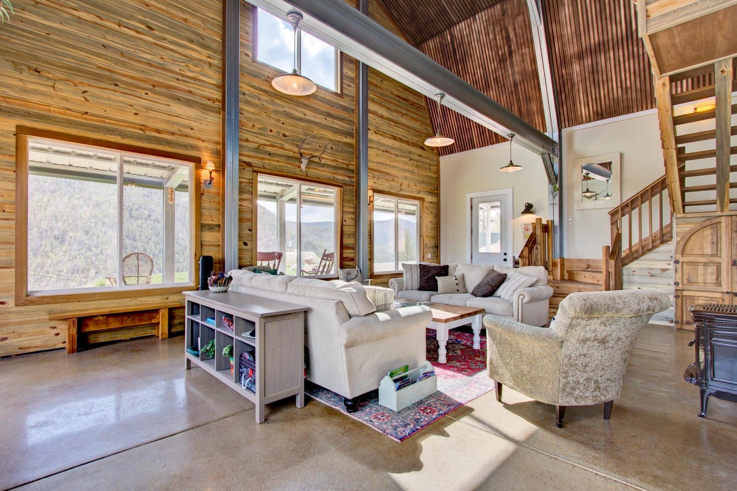 Living room with wood walls, concrete floor, white couches, and stairs.