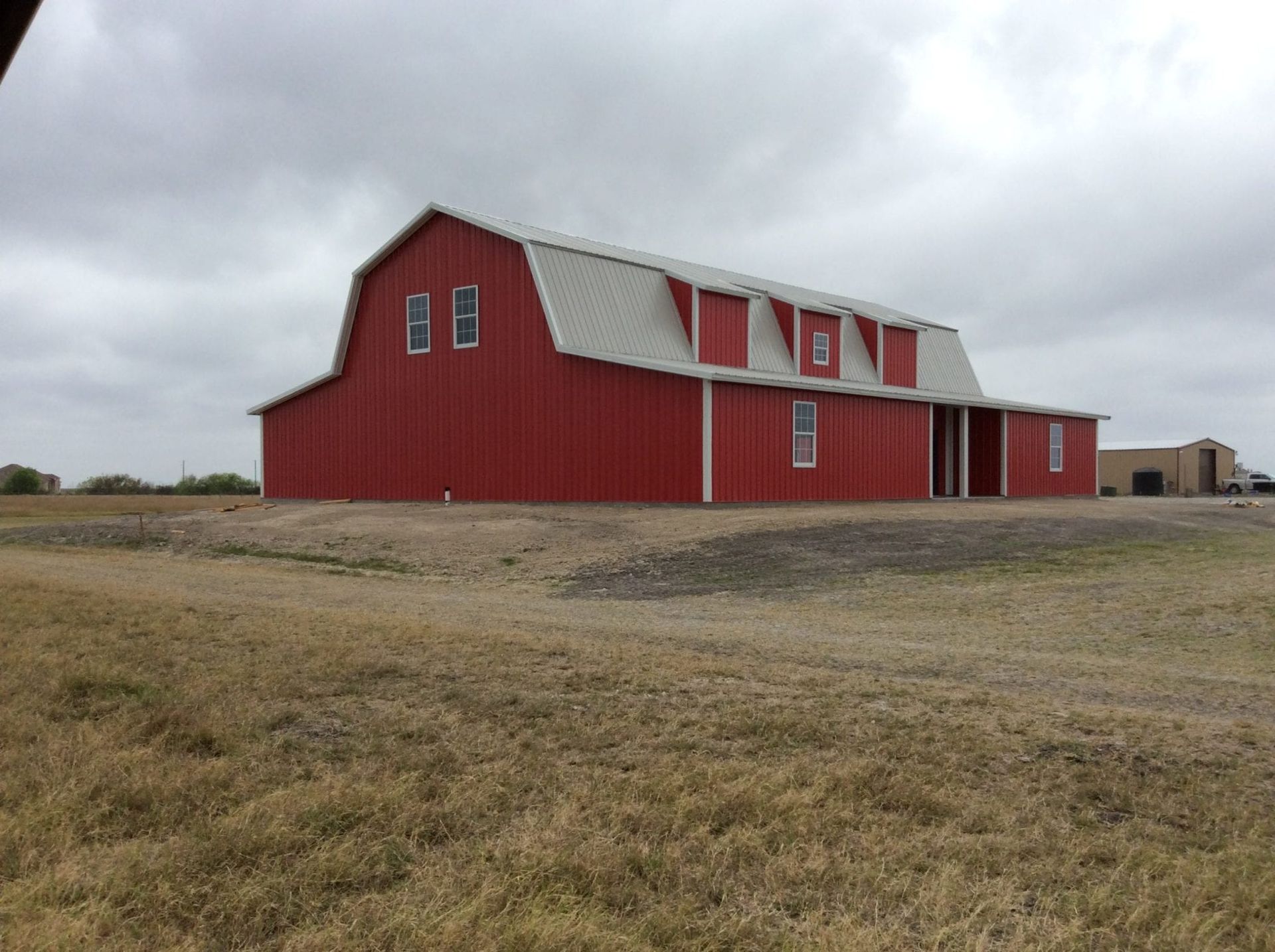 Red barn with white roof and windows, on a field, cloudy sky.