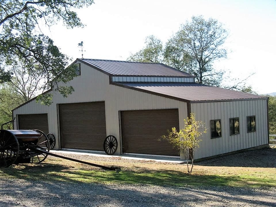 Tan metal building with brown garage doors, set in a grassy area, with a horse-drawn carriage.