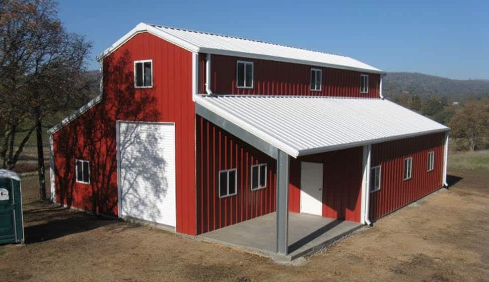Red and white barn with a porch, set against a blue sky and a hillside.