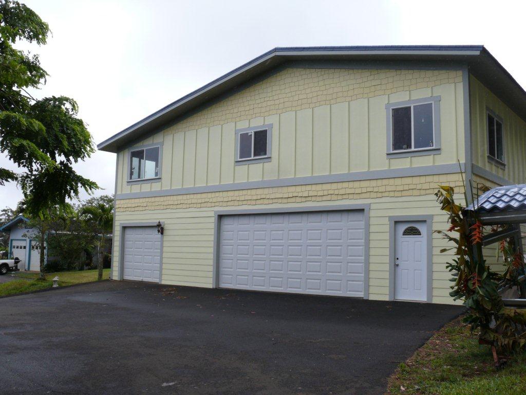 Two-story house with light yellow siding, three garage doors, and a black driveway.