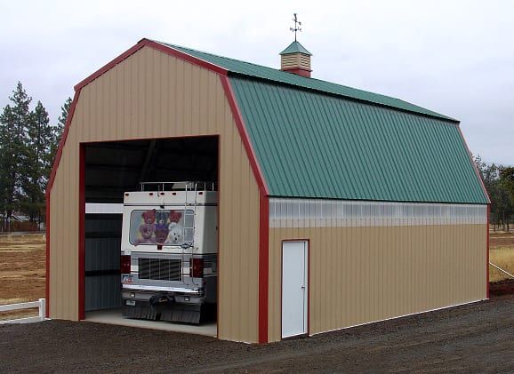 Tan barn with green roof, housing a white vehicle. Red trim, small door, overcast sky.