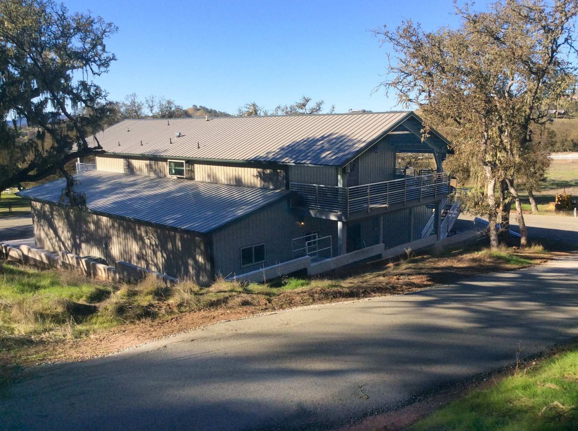 A two-story building with a metal roof, trees, and a road on a sunny day.