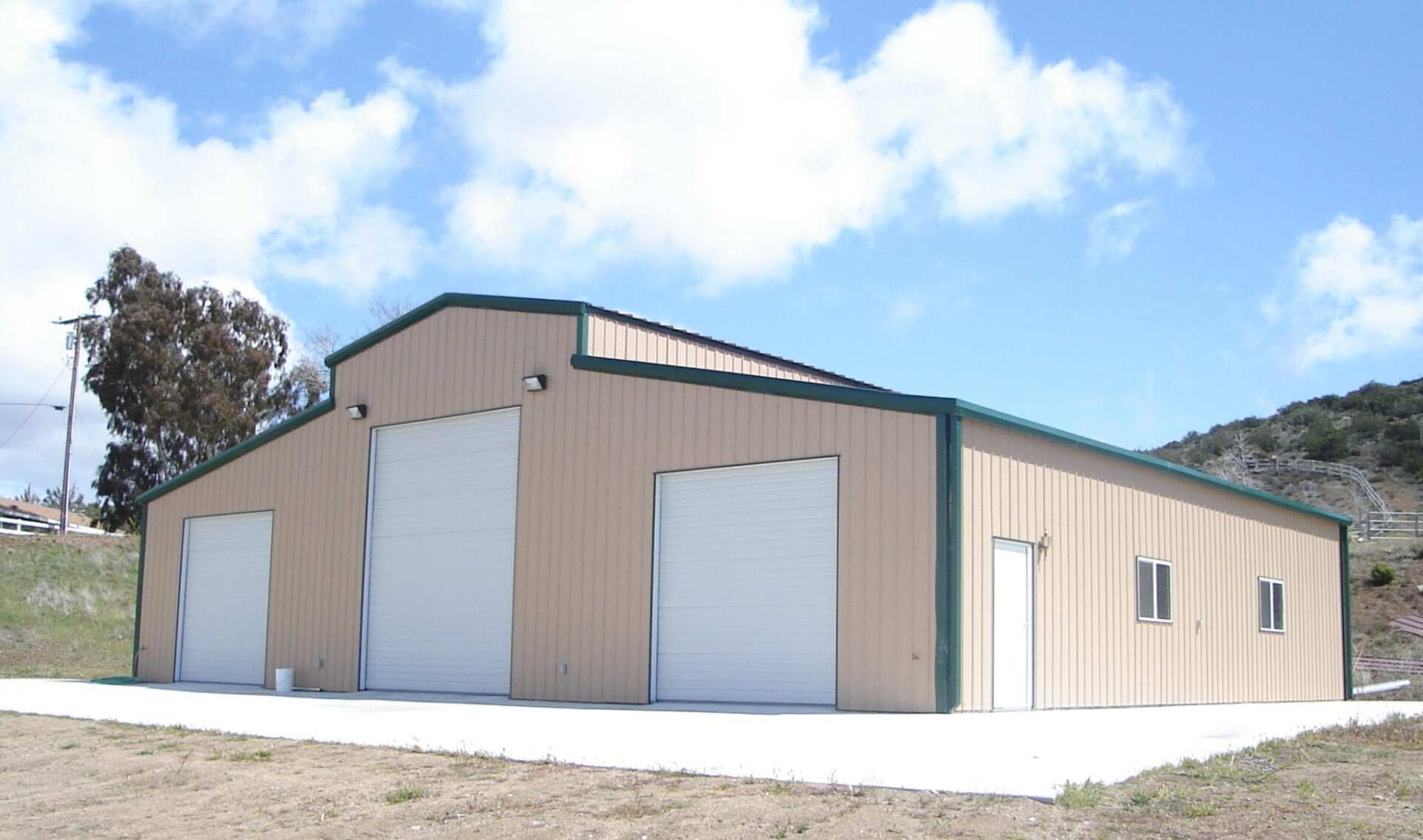 Tan metal building with three garage doors, a door, windows, and a concrete pad.