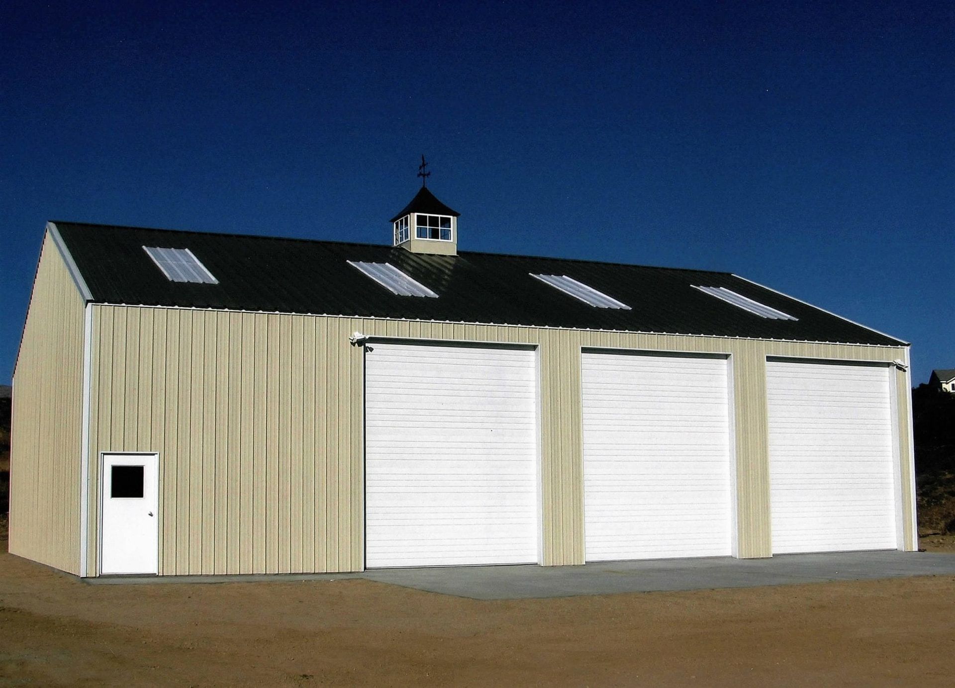 Light tan metal building with a green roof, three large garage doors, and a small door.