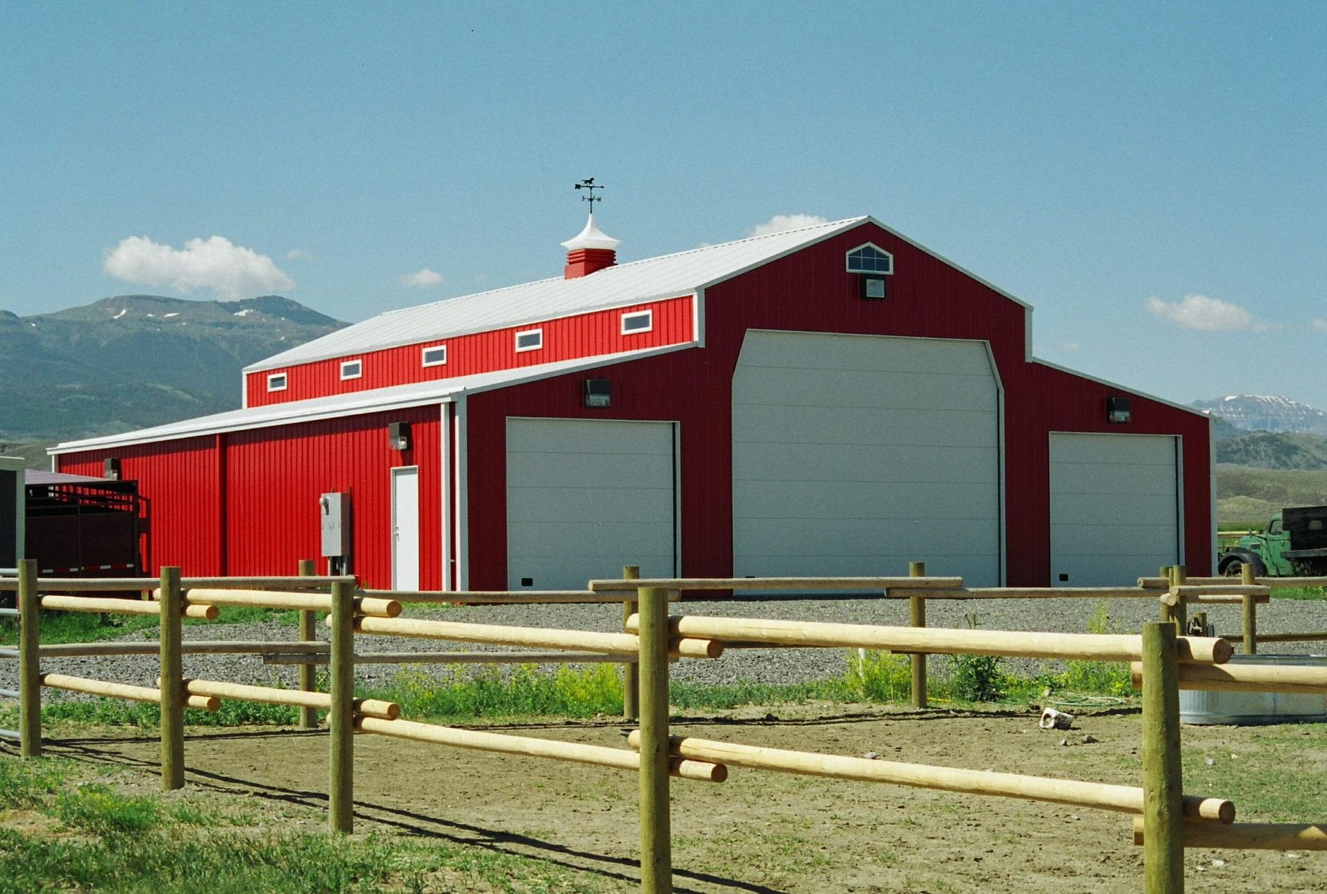 Red barn with white doors and roof against a blue sky, mountains in the background.