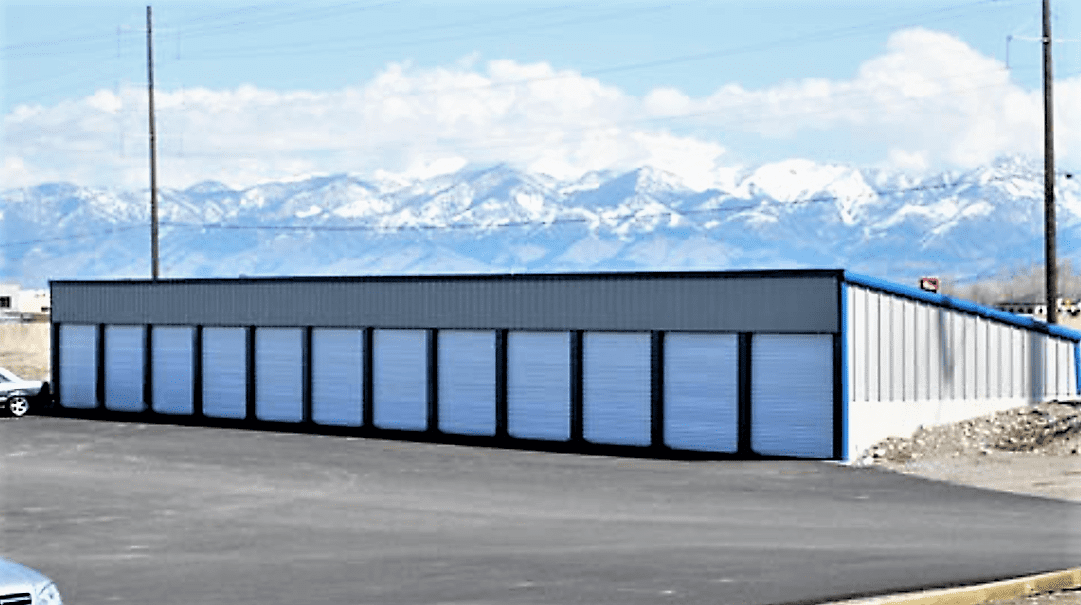Storage units with white doors, in front of snow-capped mountains, under a clear sky.