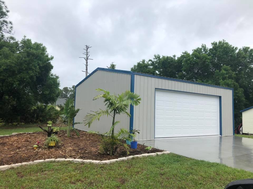Gray metal garage with white door, blue trim, and small landscaped area.