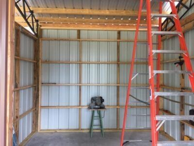Interior of a metal-walled workshop under construction; a ladder and saw are present.