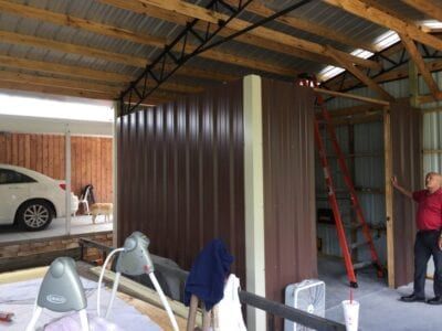 Brown metal walls being constructed inside a garage, with a person standing nearby.