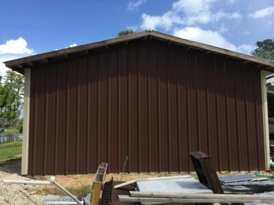 Brown metal-sided building with light-colored trim under a blue sky. Construction materials are in the foreground.
