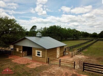 Horse barn with a gray roof, wooden exterior, and fenced pasture in a rural setting.