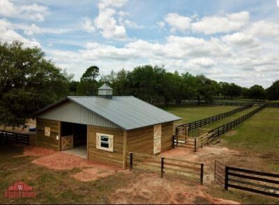 Barn with metal roof and wooden siding in a field, a fenced pasture extends in the background.