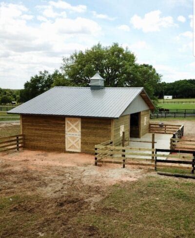 Wooden barn with silver roof and fencing on a farm.