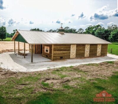 Rustic barn with weathered wood siding, metal roof, and a porch on a grassy landscape.