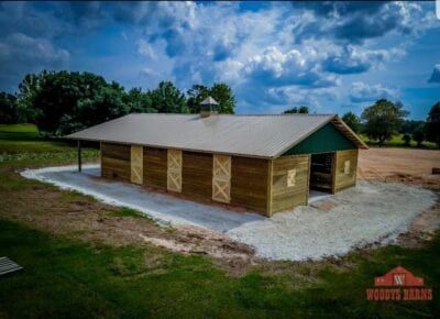 Wooden barn with metal roof, green trim, and gravel base under a cloudy sky.