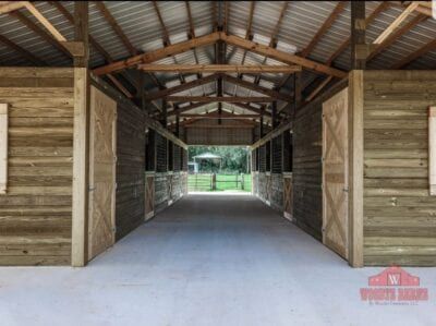 Barn interior with concrete floor, wooden stalls, and open doors leading to outdoor view.