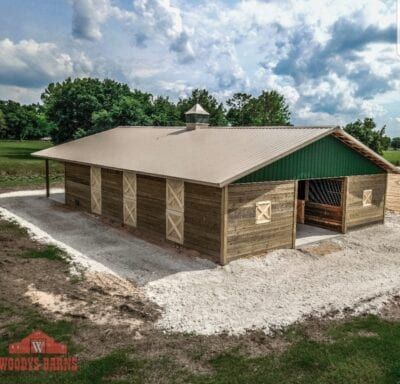 Barn with wood siding, metal roof, and open stalls. Located outdoors with cloudy sky.