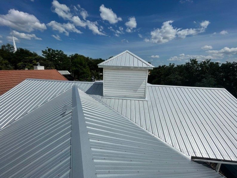 Silver metal roof with a white cupola against a blue sky with clouds.
