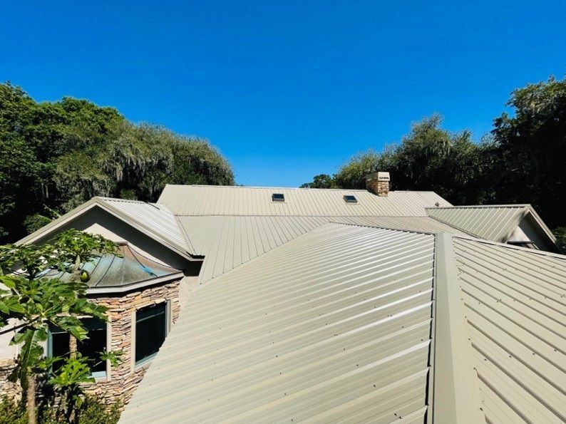 Light green metal roof on a house with trees and a clear blue sky.
