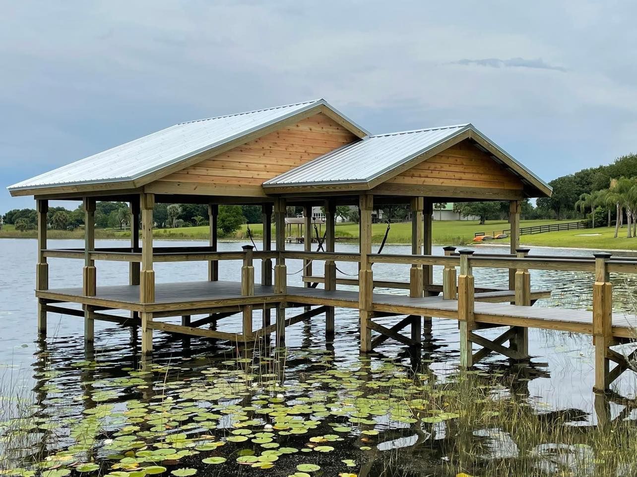 Wooden dock with a covered structure on a lake under a cloudy sky.