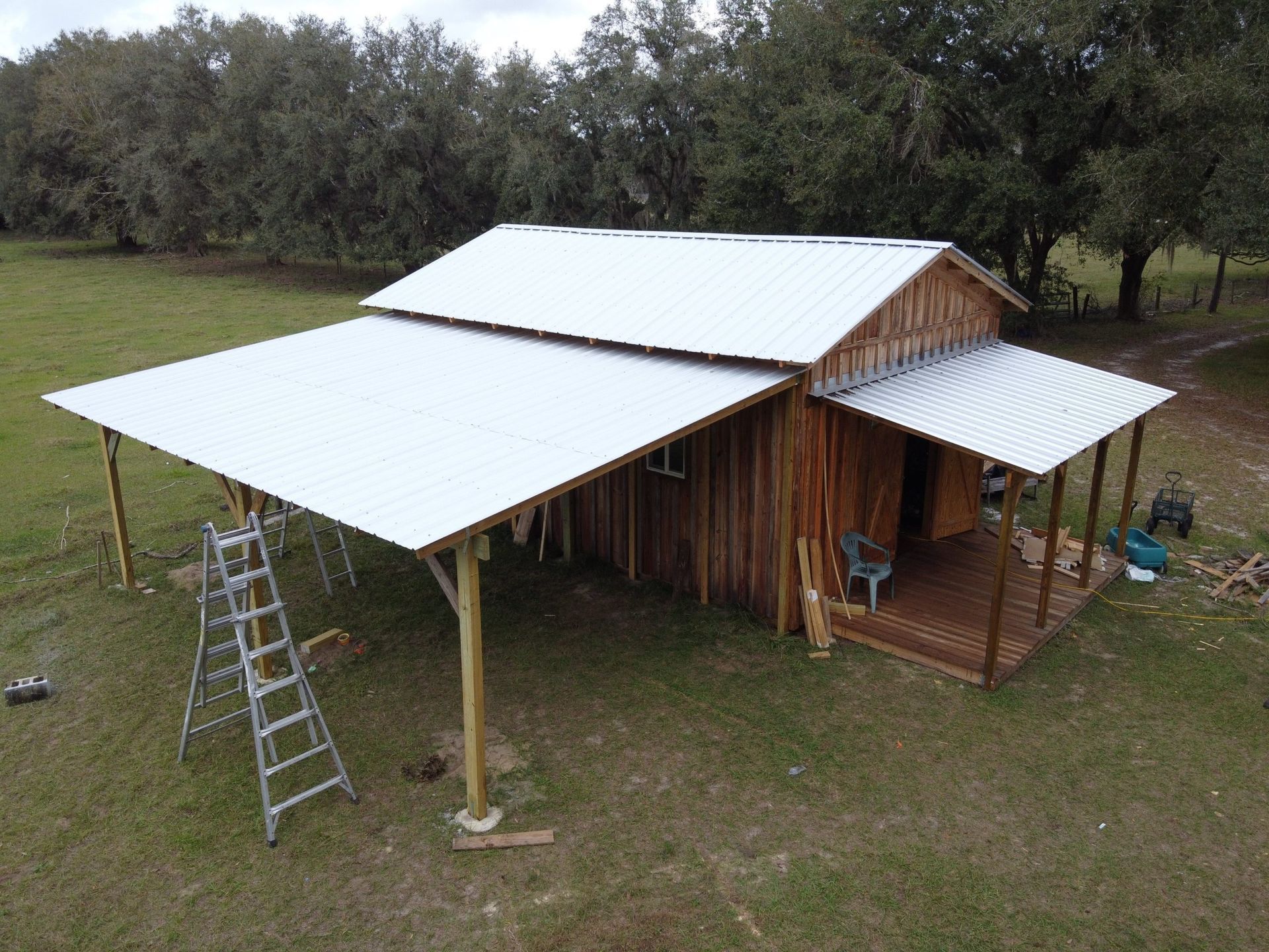 Rustic wooden cabin with a large white metal roof and a porch, in a grassy field.