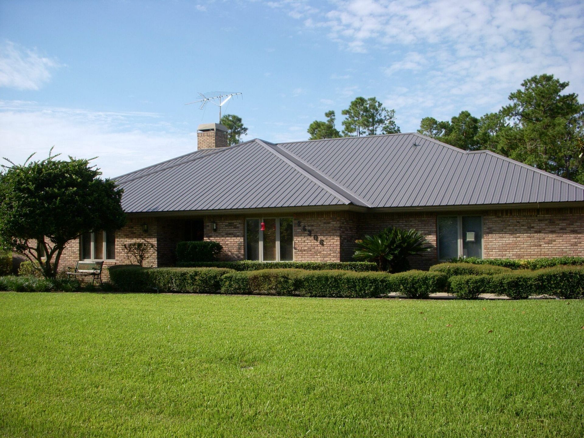 Brick house with a gray roof, green lawn, and hedges.