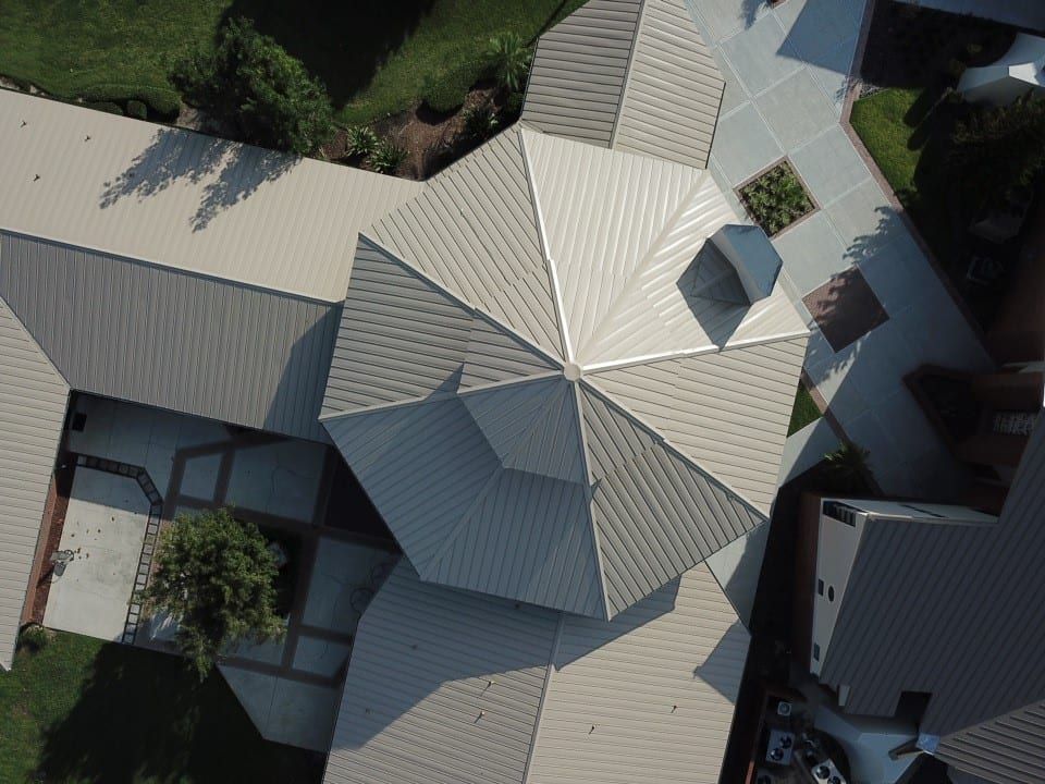 Overhead view of a building with a multi-faceted roof. Light beige metal roof with a central tower and surrounding buildings.