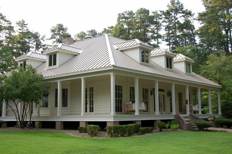 White two-story house with porch and dormers, set in a green yard, surrounded by trees.