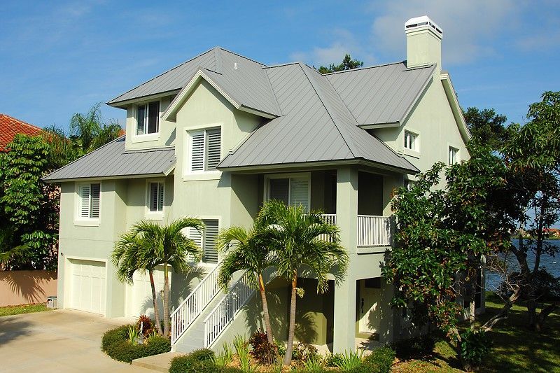 Green house with gray roof, palm trees, and sunny sky.