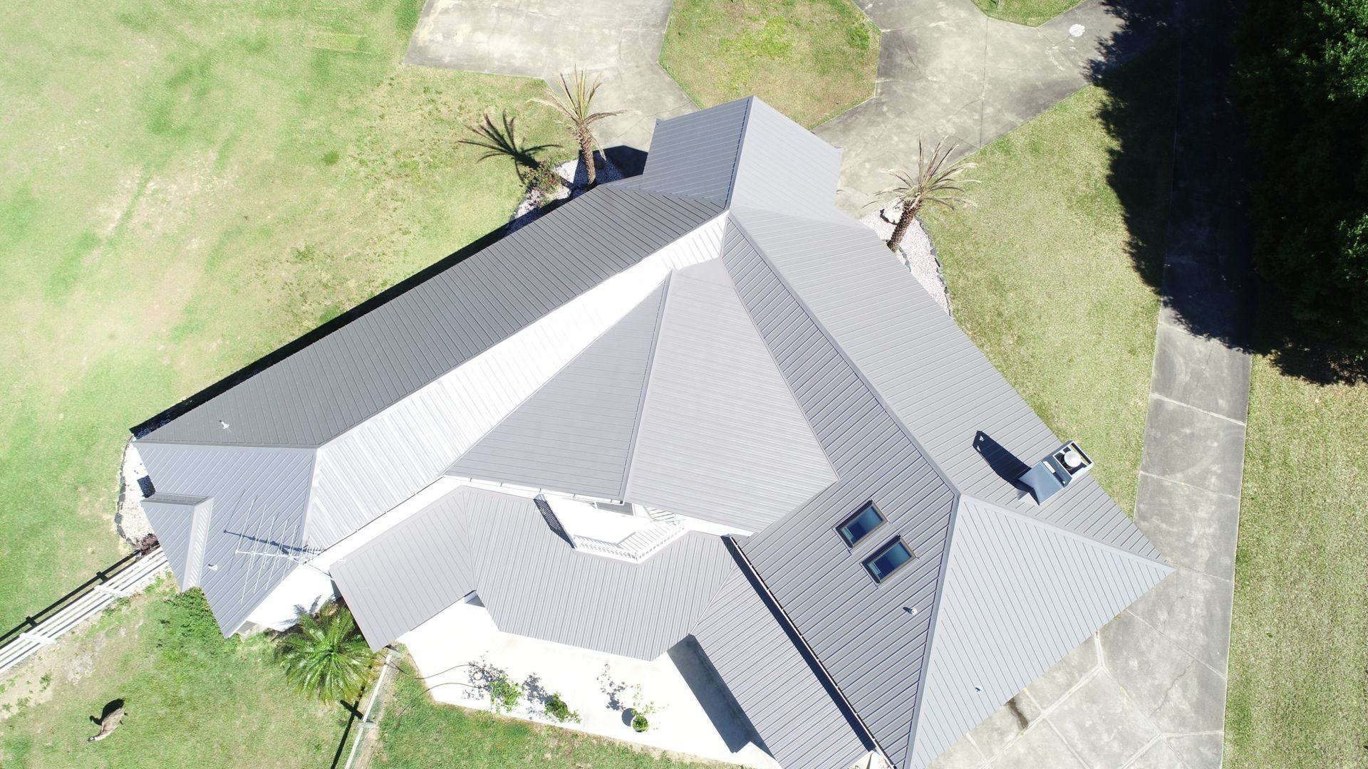 Overhead view of a house with a complex gray roof, surrounded by green grass and a concrete driveway.