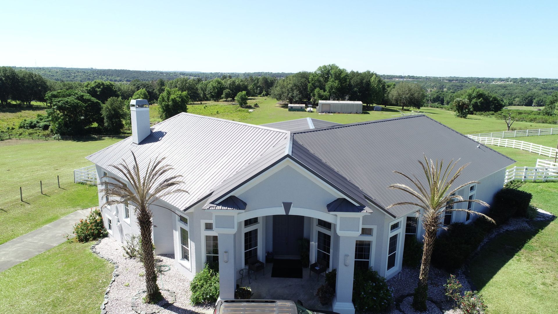 House with gray metal roof, palm trees, and a rural setting.