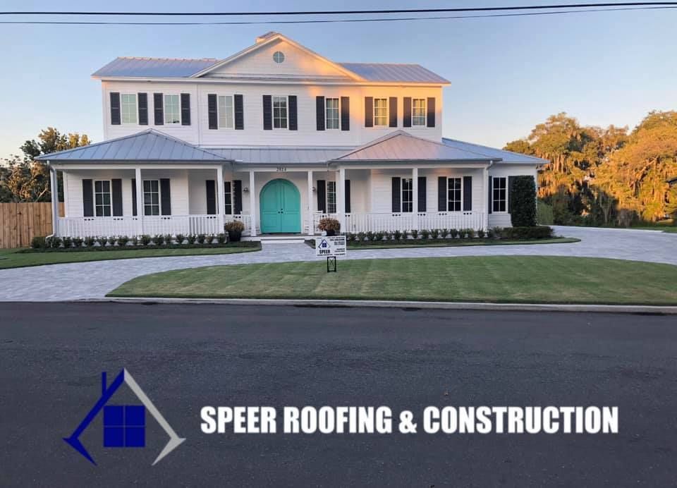 White two-story house with metal roof, turquoise door. Speer Roofing & Construction logo in the foreground.