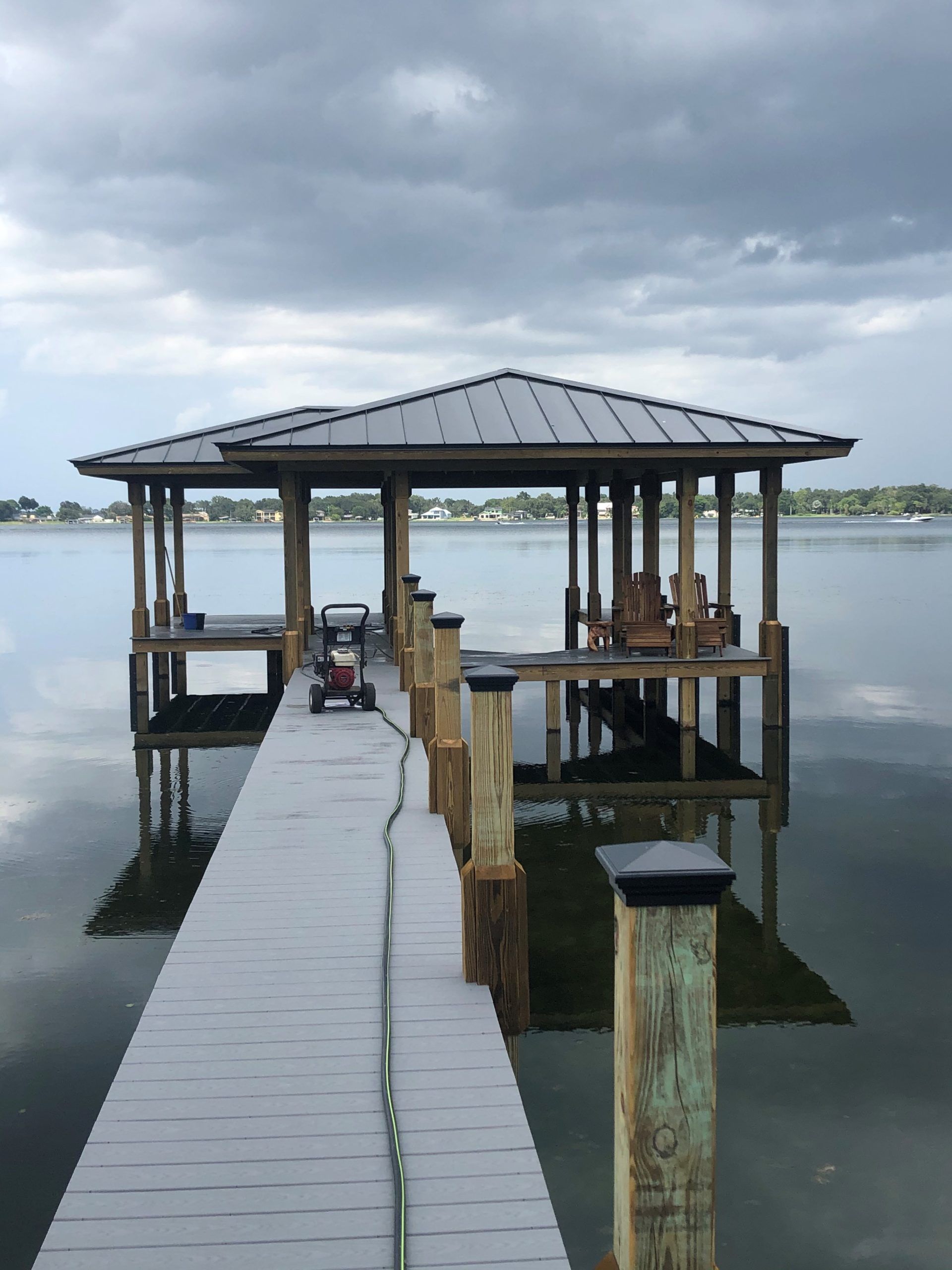 Dock with covered seating area on calm water under cloudy sky.