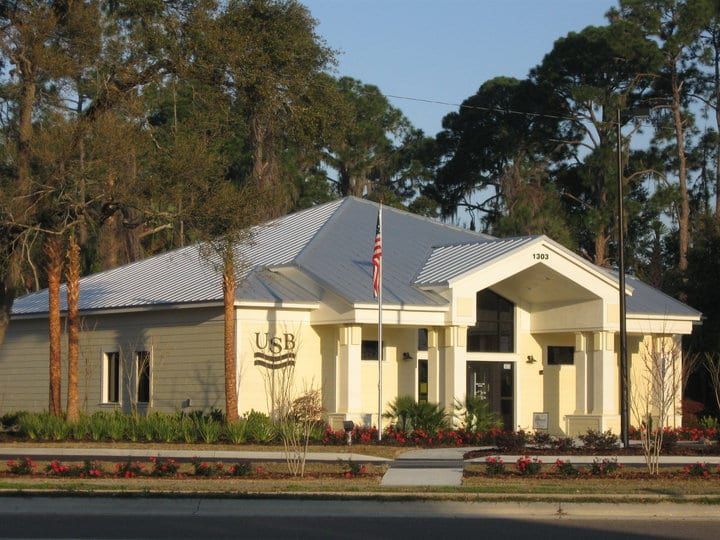 A light yellow US Bank building with a silver roof and an American flag in front.