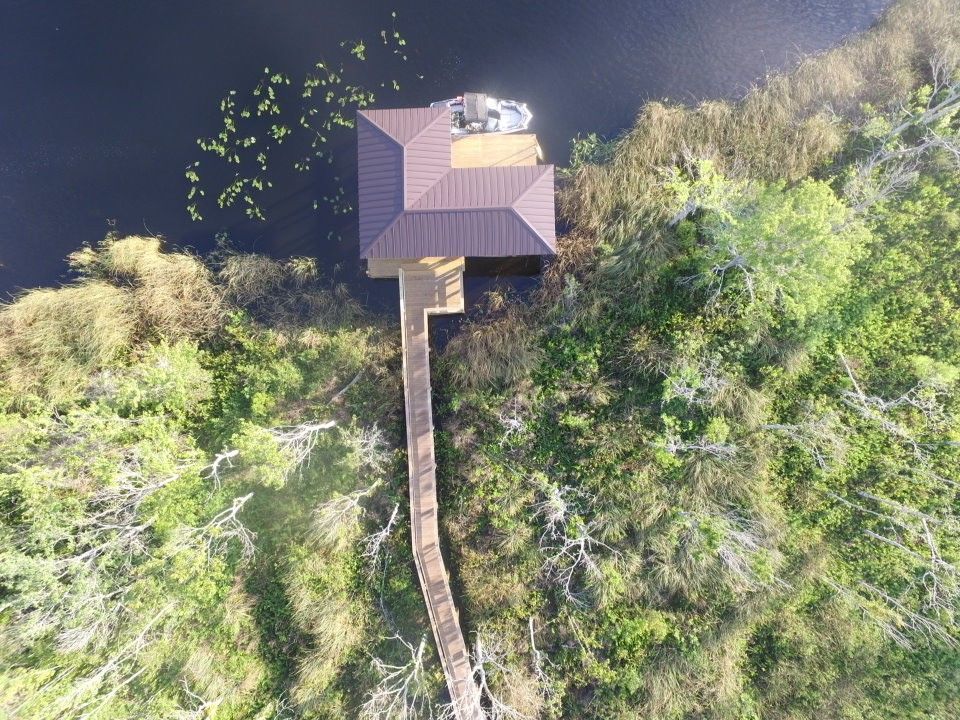 Aerial view of a dock and covered boat slip on a lake, surrounded by green marsh and trees.