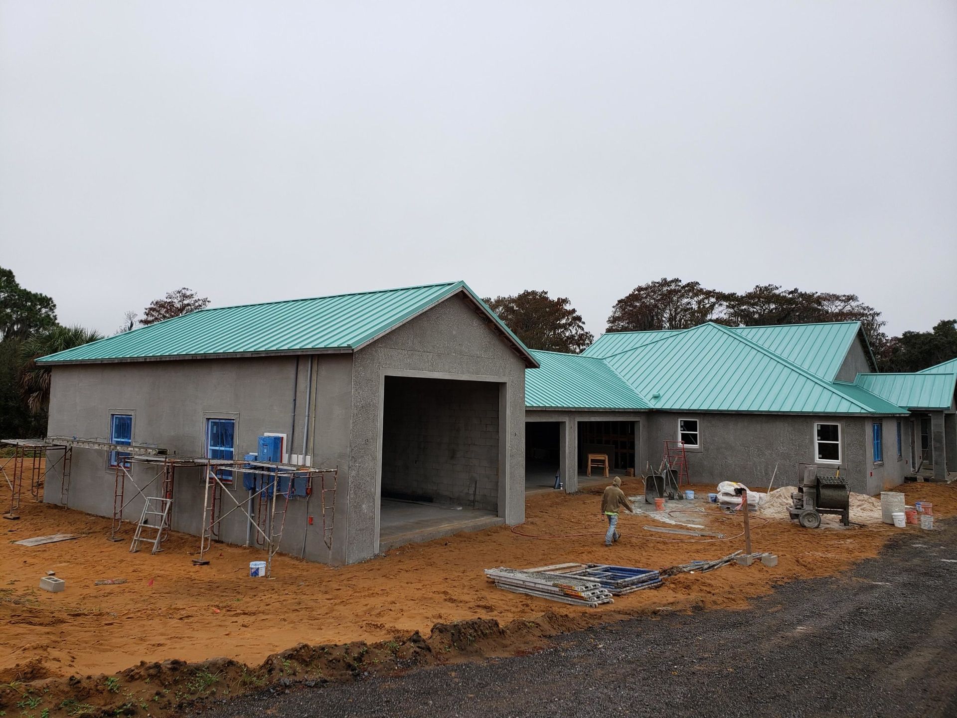 Construction site with gray concrete buildings, turquoise roofs, and a cloudy sky.