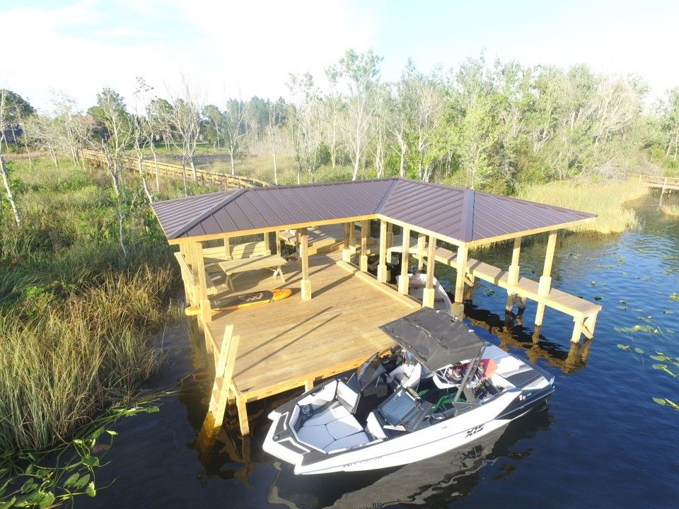 A wooden dock with a covered boat slip on a lake. A boat is docked. Trees are in the background.
